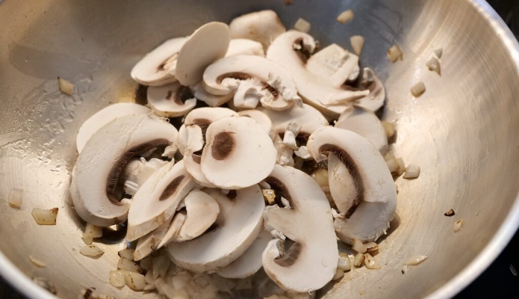 Sliced mushrooms in the pan with the onion